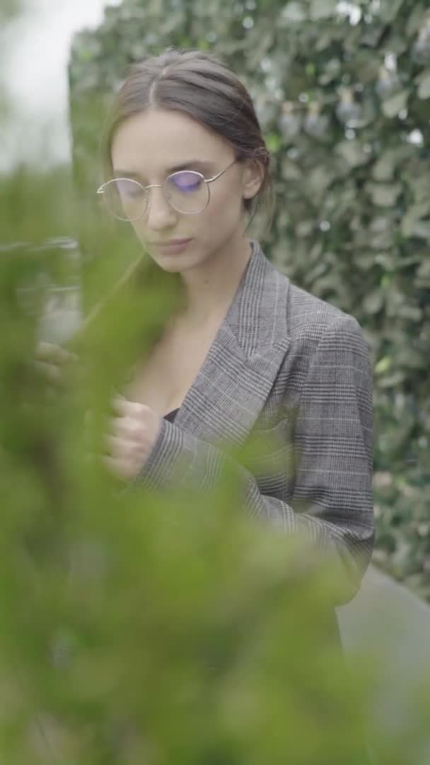 Vídeo vertical. Hermosa chica en gafas y un traje gris. Movimiento lento — Vídeos de Stock