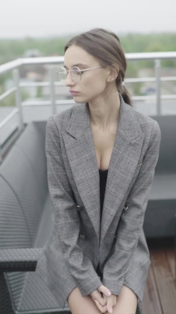 Dikey video. Gözlüklü ve gri takım elbiseli güzel bir kız. Yavaş çekim — Stok video