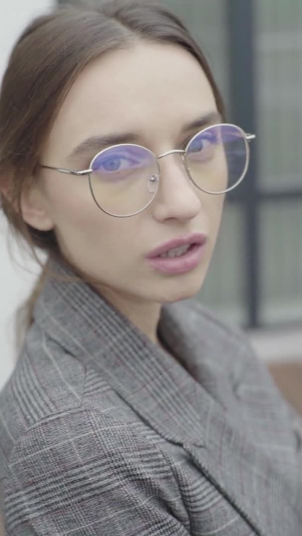 Vertikal video. Vacker tjej i glasögon och grå kostym. Långsamma rörelser — Stockvideo