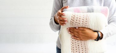 Kadın eli, beyaz bir arka planda, hafif doğal iplikten elde örülmüş ekose kumaşlar tutuyor..