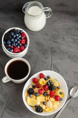 Beyaz tabakta mısır gevreğiyle sağlıklı kahvaltı. Koyu gri arka planda böğürtlen, süt ve kahve..