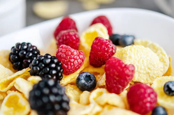 Здоровий сніданок з кукурудзяними пластівцями в білій тарілці, ягодами, молоком та горіхами на темно-сірому фоні . — стокове фото