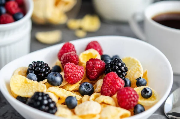 Здоровий сніданок з кукурудзяними пластівцями в білій тарілці, ягодами, молоком та горіхами на темно-сірому фоні . — стокове фото
