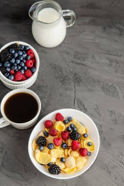 Beyaz tabakta mısır gevreğiyle sağlıklı kahvaltı. Koyu gri arka planda böğürtlen, süt ve kahve..