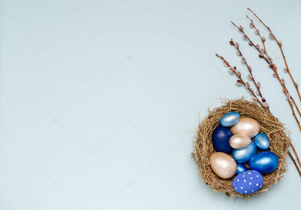 Easter eggs in blue tones in a nest of straw with willow branches on a blue background with place for copy space.