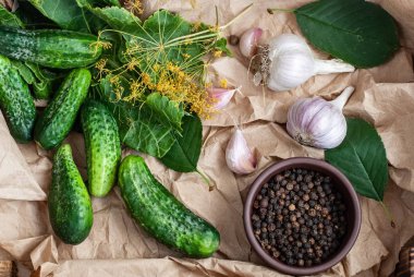 Çiğ salatalıklar, dereotu çiçekleri, kiraz yaprağı, yabanturpu yaprağı, baharatlar ve otlar ahşap bir arka planda bir tepside..