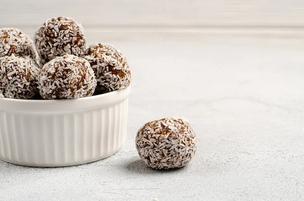 Bolas de energía de dátiles, nueces, avena, espolvoreado con polvo de coco primer plano en un plato blanco sobre un fondo blanco con espacio para copiar — Foto de Stock