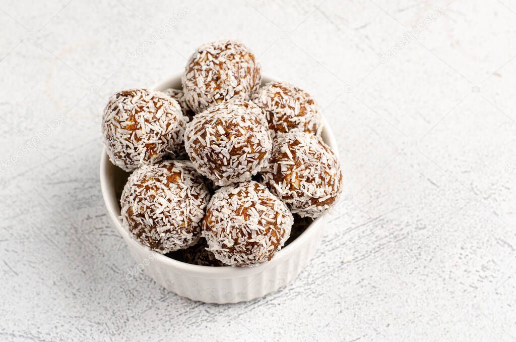 Energy balls of dates, nuts, oats, sprinkled with coconut powder closeup in a white plate on a white background background with copy space with place for text.