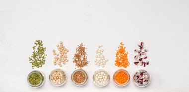 Cam kavanozlardaki vejetaryenler için çeşitli kuru tahıllar: mercimek, nohut, fasulye, beyaz arka planda karabuğday. Uzayı kopyala Yüksek miktarda protein ve karbonhidrat içeren sağlıklı yiyecekler. Yukarıdan görüntüle.