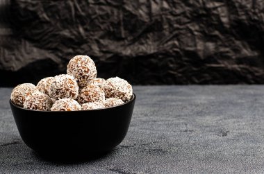 Ev yapımı enerji topları, yer fıstığı, yulaf, siyah bir arka planda hindistan cevizi serpiştirilmiş, metin için yer olan fotokopi alanı. Çiğ tatlı, sağlıklı ve sağlıklı bir atıştırmalık. Yakın plan.