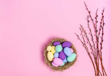 Easter eggs colored in a decorative nest of straw and pussy-willow branches on a pink background, copy space, flat lay
