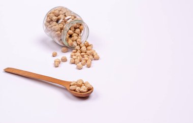 Tahta kaşıkta vejetaryenler için kuru nohut ve beyaz arka planda cam bir kavanoz, fotokopi alanı, mesaj için yer. Yüksek miktarda protein ve karbonhidrat içeren sağlıklı yiyecekler. Yakın plan..