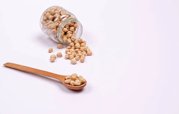 Tahta kaşıkta vejetaryenler için kuru nohut ve beyaz arka planda cam bir kavanoz, fotokopi alanı, mesaj için yer. Yüksek miktarda protein ve karbonhidrat içeren sağlıklı yiyecekler. Yakın plan..