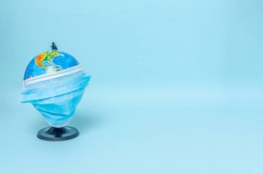 Mavi arka planda koruyucu bir tıbbi maske takan küçük bir küre. Coronovirus, Covid-19, Karantina, Salgın. Yakın plan. Düz konum, kopyala boşluk, boşluk için boşluk.