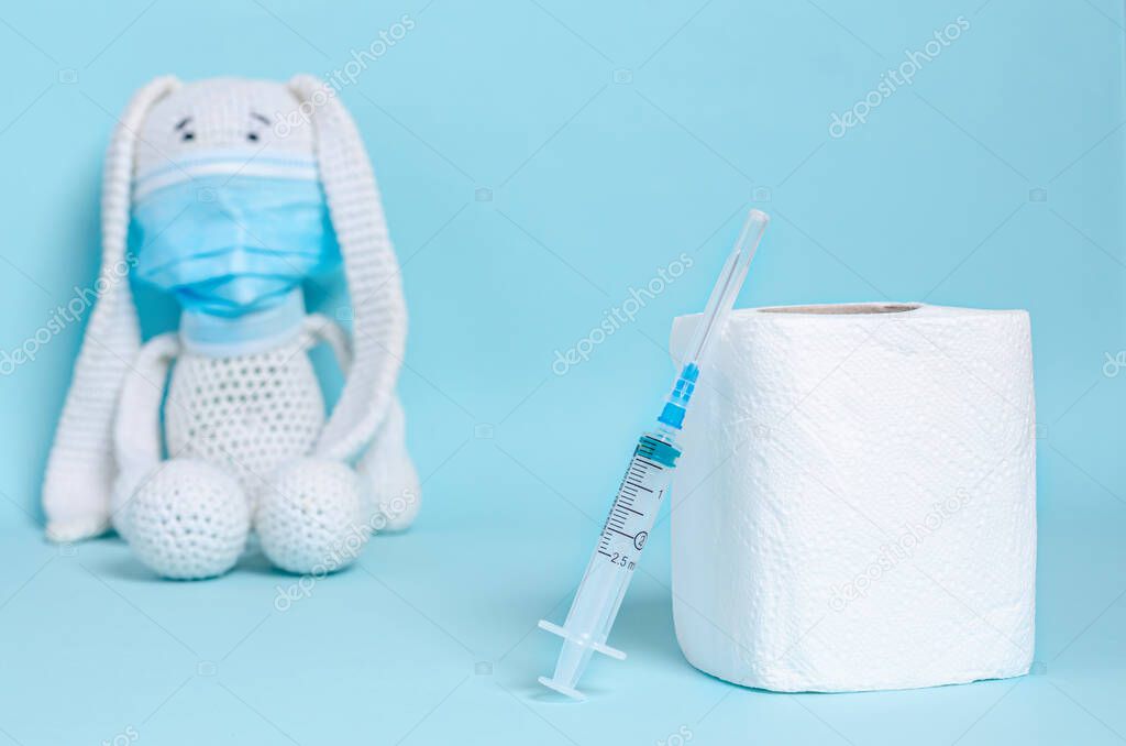 Toilet paper and syringe, children's soft toy bunny in a protective medical mask on a blue background. Coronovirus, Covid-19, Quarantine, Pandemic. Close-up. Flat lay, copy space.