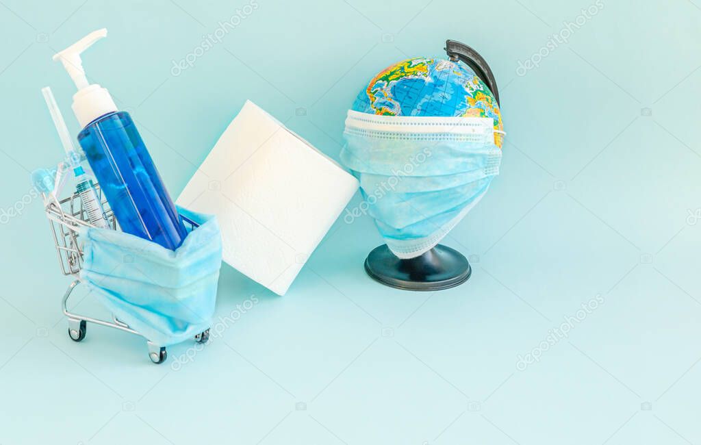 Decorative small basket with a protective medical mask, syringe, soap in the bank, toilet paper, globe with a mask on a blue background. Coronovirus, Covid-19, Pandemic. Close-up. Flat lay, copy space
