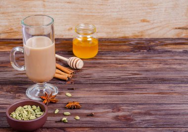 Geleneksel Hint çayı Masala çayı, uzun cam bardakta. Çay yapmak için gerekli malzemeler. Tarçın, bal, kakule, anason, ahşap arka planda karanfil. Yakın plan. Boşluğu, düzlüğü, metin için boşluk kopyala.