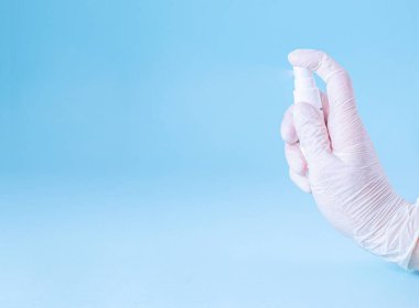 Lastik beyaz eldivenli bir kadın, mavi arka planda beyaz bir şişeden antiseptik püskürtüyor. Pankart. Coronovirus, Covid-19, Karantina, Salgın. Yakın plan. Düz yat, boşluğu kopyala.