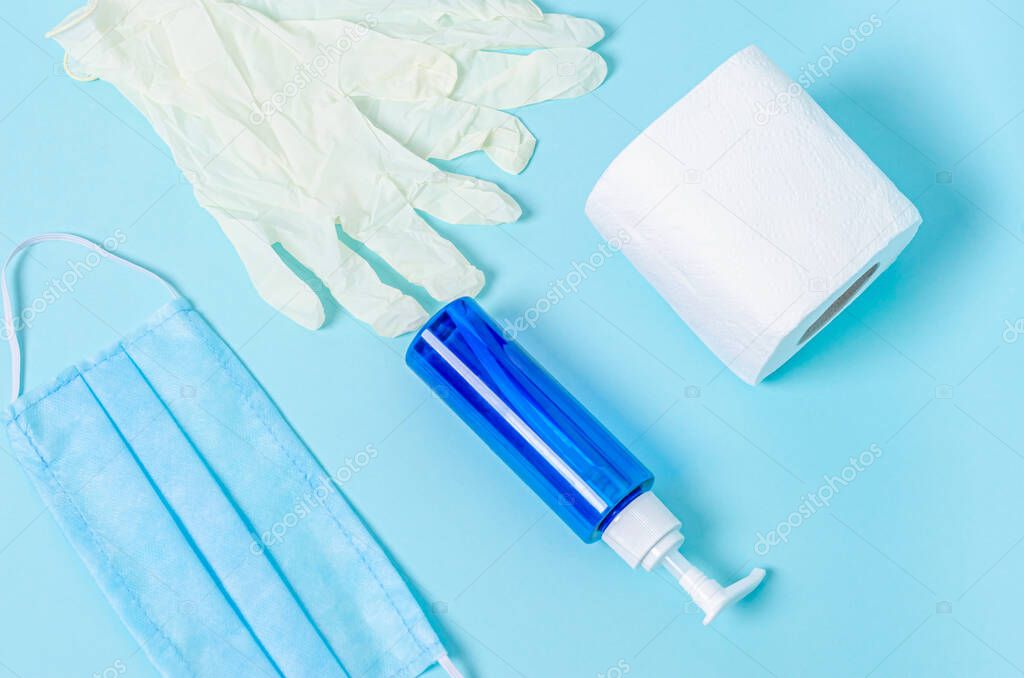 Jar with liquid soap, toilet paper, protective medical mask, white rubber gloves on a blue background. Coronovirus, Covid-19, Quarantine, Pandemic. View from above. Flat lay, copy space.