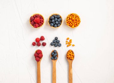 Olgun ahududu böğürtlen, yaban mersini, beyaz arka planda tahta kaşıklarda deniz dikenleri. Boşluğu, düzlüğü, metin için yeri kopyala. Doğal tatlı, sağlıklı atıştırmalık. Yukarıdan görüntüle.