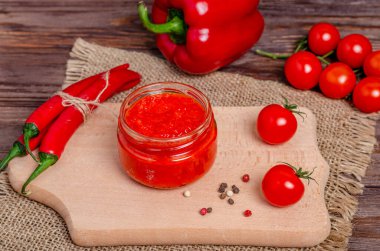 Ayvar ya da pindjur kırmızı sebze ezmesi ya da kırsal bir ahşap masanın üzerindeki bir kesme tahtasındaki cam kavanozda biber biberi ve domates kreması. Sırp yerlisi, geleneksel yemekler. Uzayı kopyala Yakın plan..