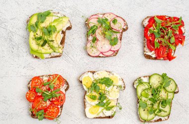 Hafif arka planda krem peynirli ve sebzeli mini sandviçler. Peynirli sandviç, salatalık, turp, domates, tatlı biber, avokado, yumurta, mikroyeşil, üst manzara. Düz yatıyordu