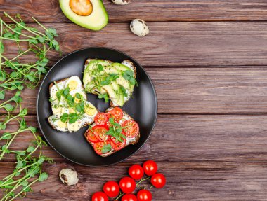Siyah tabakta krem peynirli ve sebzeli mini sandviçler. Peynirli sandviçler, domatesler, avacado, yumurta, ahşap arka planda mikroyeşil. Düz konum, kopyala boşluk. Yakın çekim, üst görünüm