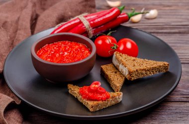 Ayvar ya da pindjur kırmızı sebze ezmesi ya da kırmızı biber biberi ve domates kremasını siyah bir tabakta, kırsal bir ahşap masada. Sırp yerlisi, geleneksel yemekler. Yakın plan.