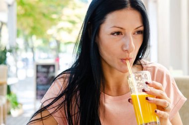 Genç bir kız temiz havadaki bir pipetle cam bardaktan taze portakal suyu içiyor. Sağlıklı beslenme, doğal ürün, sağlıklı atıştırmalık..