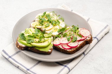 Gri tabakta krem peynirli ve sebzeli mini sandviçler, açık arkaplan. Peynirli sandviç, turp, avkado, yumurta, mikroyeşil. Sağlıklı atıştırmalıklar. Uzayı kopyala, düz yat. Yakın plan.