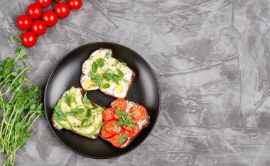 Siyah tabakta krem peynirli ve sebzeli mini sandviçler, koyu arkaplan. Peynirli sandviç, avkado, yumurta, domates, mikroyeşil, üst manzara. Uzayı kopyala Düz yatıyordu. Metin için yer