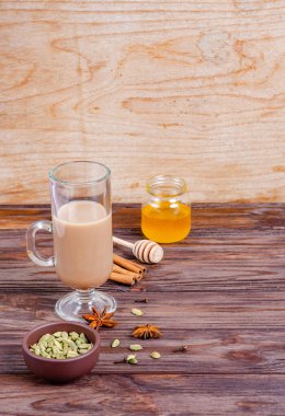 Geleneksel Hint çayı Masala çayı, uzun cam bardakta. Çay yapmak için gerekli malzemeler. Tarçın, bal, kakule, anason, ahşap arka planda karanfil. Yakın plan. Boşluğu, düzlüğü, metin için boşluk kopyala.