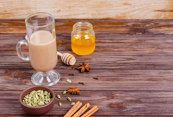 Geleneksel Hint çayı Masala çayı, uzun cam bardakta. Çay yapmak için gerekli malzemeler. Tarçın, bal, kakule, anason, ahşap arka planda karanfil. Yakın plan. Boşluğu, düzlüğü, metin için boşluk kopyala.