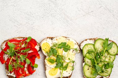 Hafif arka planda peynirli ve sebzeli mini sandviçler. Peynirli sandviç, yumurta, salatalık, tatlı biber, mikroyeşil, üst manzara. Sağlıklı atıştırmalıklar. Uzayı kopyala, düz yat.