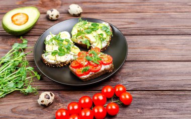 Siyah tabakta krem peynirli ve sebzeli mini sandviçler. Peynirli sandviç, domates, avokado, yumurta, ahşap arka planda mikroyeşil. Düz konum, kopyalama alanı. Yakın plan.