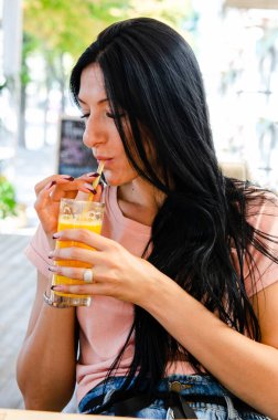 Genç bir kız temiz havadaki bir pipetle cam bardaktan taze portakal suyu içiyor. Sağlıklı beslenme, doğal ürün, sağlıklı atıştırmalık..