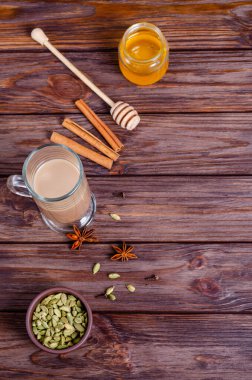 Geleneksel Hint çayı Masala çayı, uzun cam bardakta. Çay yapmak için gerekli malzemeler. Tarçın, bal, kakule, anason, ahşap arka planda karanfil. Yukarıdan bak. Boşluğu, düzlüğü, metin için boşluk kopyala