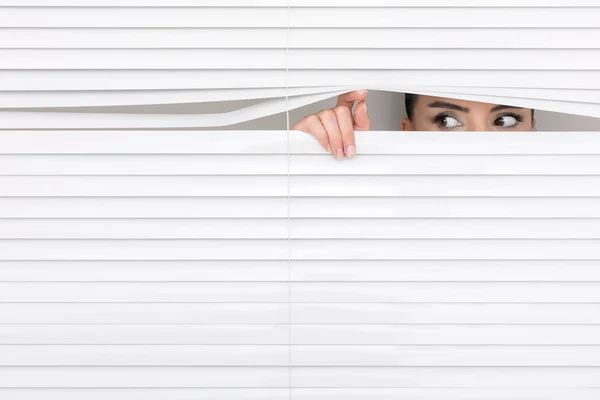 Portrait of a woman looking through out the blinds — Stock Photo, Image
