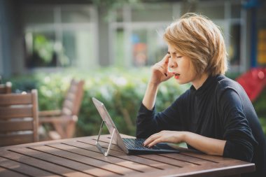 Asyalı kadın dizüstü bilgisayar başında çalışırken baş ağrısı çekiyor..
