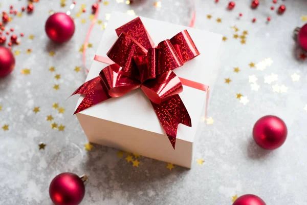 Wit cadeau met rode strik op grijze achtergrond met kerstboom speelgoed ballen en confetti. vlakke lay — Stockfoto