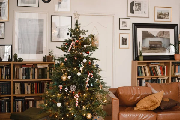 Kerstboom met speelgoed, decoraties en bloemenslingers, verlichting in een bruine stijlvolle kamer. Nieuwjaar warm stijlvol interieur — Stockfoto