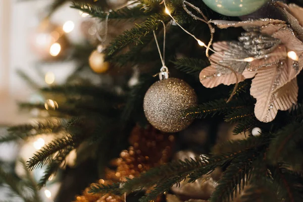 Beige Weihnachtskugel auf einem Weihnachtsbaum in einem hellen Inneren vor dem Hintergrund brennender Lichterketten. Weihnachtsbaum schmücken auf hellem Hintergrund — Stockfoto