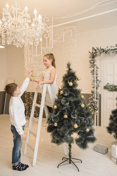 Los niños pequeños decoran el árbol de Navidad en un interior brillante. Chica y niño, hermano y hermana cuelgan juguetes de Año Nuevo en las ramas de abeto. Familia Navidad y Año Nuevo concepto —  Fotos de Stock