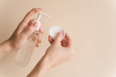 Kız deriyi temizlemek için pamuğa mikiler jeli döküyor. Kızın elleri pamuk pedin üzerine su sıkıyor.