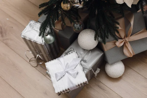 Brillantes regalos de plata en el embalaje y con lazos bajo el árbol de Navidad en el suelo. Decoraciones navideñas. Fondo de Navidad. Hermosa habitación decorada de vacaciones con árbol de Navidad con regalos un — Foto de Stock