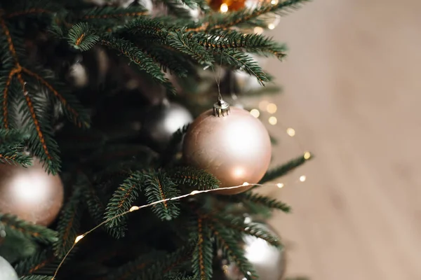 Beżowa świąteczna piłka na choince w jasnym wnętrzu na tle płonących girland świateł. Dekorowanie choinki na jasnym tle — Zdjęcie stockowe