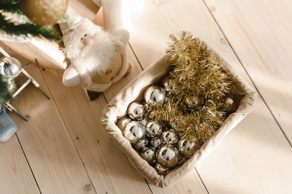 Korb mit Weihnachtskugeln und Spielzeug unter dem Weihnachtsbaum. Vorbereitungen für das Schmücken des Weihnachtsbaums. Silberne und goldene Kugeln, Lametta mit Schachtel auf Holzboden — Stockfoto