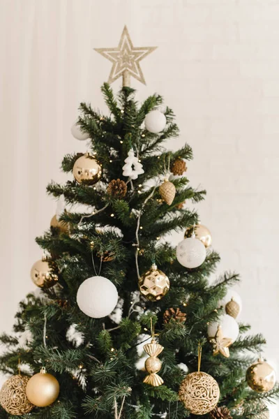 De top van een kerstboom die thuis staat. Beige gouden glanzende ster aan de top van de boom. Decoratie van een kerstboom met beige, gouden en witte kerstballen en decoraties — Stockfoto
