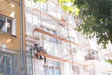 Bir adam oturuyor ve binayı restore ediyor. İnşaatçı binanın duvarlarını ve ön cephesini boyar.