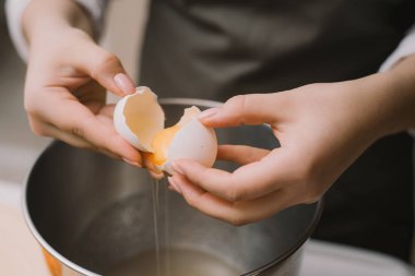 Gri önlüklü kadın aşçı metal bir kasede yumurta kırıyor. Proteini sarısından ayır.